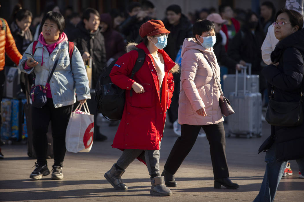 Travelers wear face masks as they walk outside of the Beijing Railway Station in Beijing, Monda ...