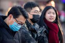 Travelers wear face masks as they walk outside of the Beijing Railway Station in Beijing, Monda ...
