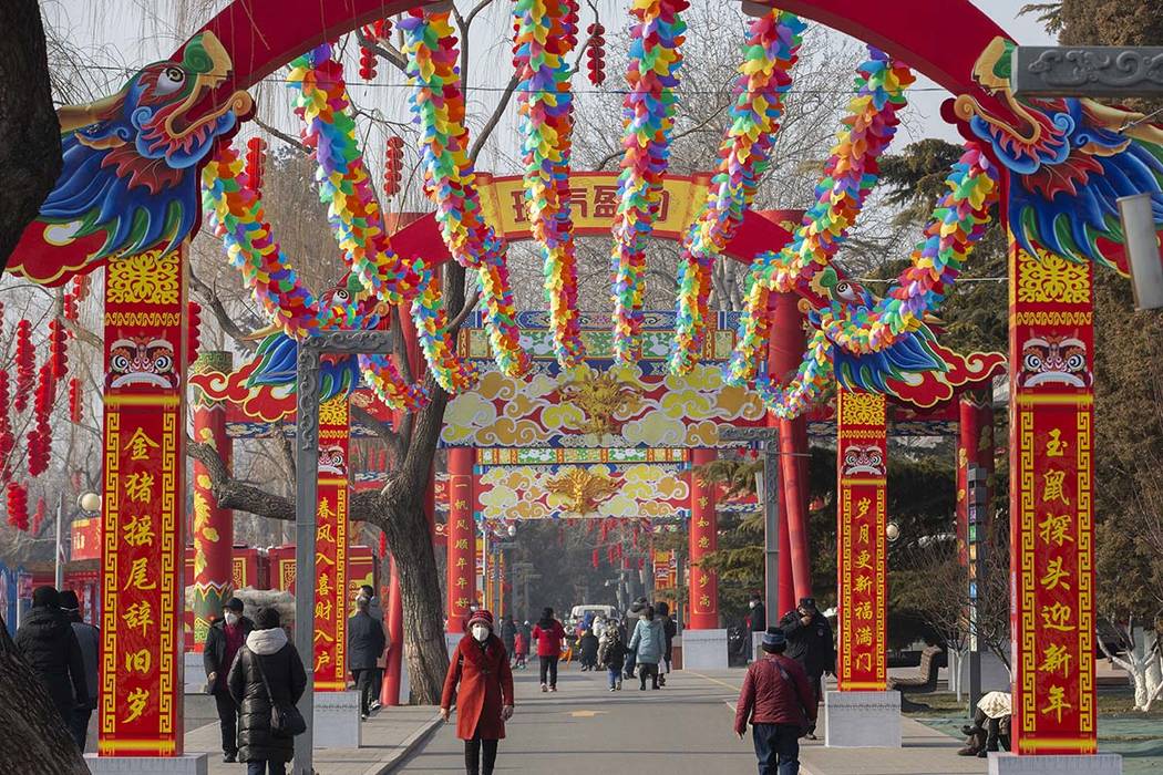 People wearing face masks walk under a canopy decorated with spinning colored fans for a cancel ...
