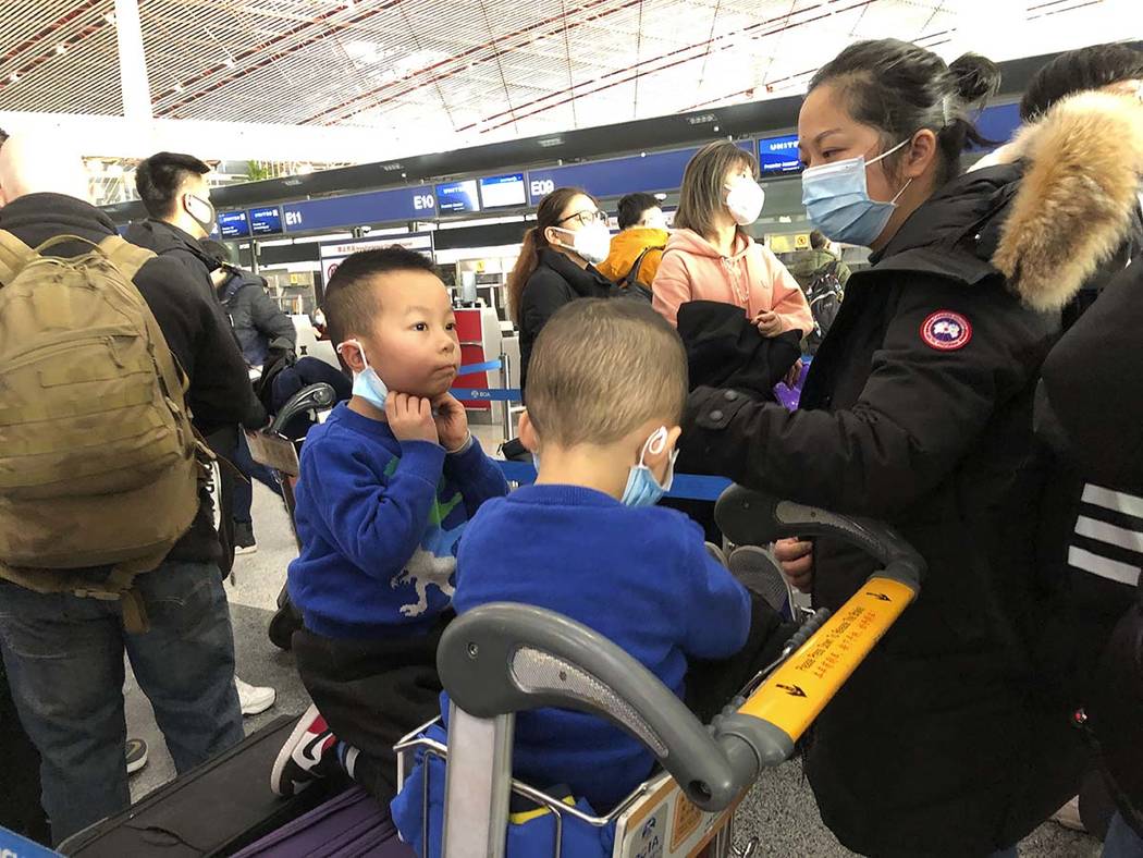 Children adjust their face masks as they wait in line at check-in counters at Beijing Capital I ...