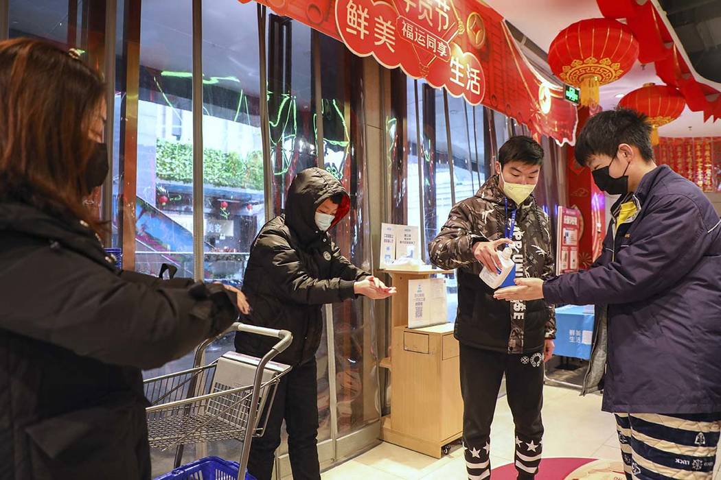 A worker dispenses hand sanitizer to shoppers at the entrance of a supermarket in Wuhan in cent ...