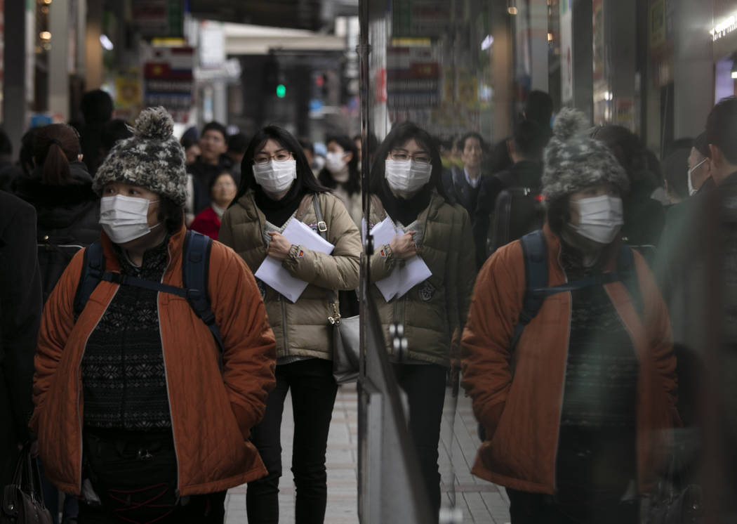 Commuters wearing protective face masks walk on a sidewalk Monday, Jan. 27, 2020, in the Shinju ...