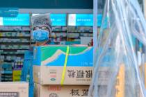 A clerk wearing a face mask and a plastic bag stands in a pharmacy in Wuhan in central China's ...