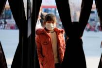 A girl wearing a face mask stands in the entrance to a shop in Wuhan in central China's Hubei P ...