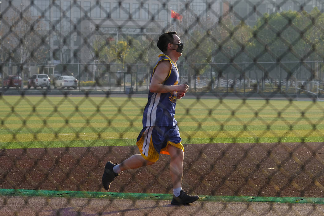 A man wearing a face mask jogs along a track in Wuhan in central China's Hubei Province, Friday ...