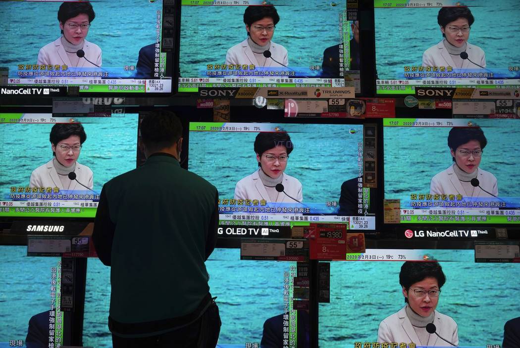 A man wears protective face masks stands in front of TV screens broadcasting Hong Kong Chief Ex ...