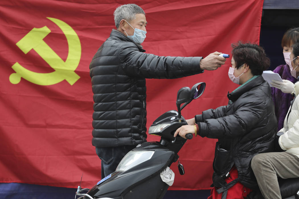 A volunteer stands in front of a Communist Party flag as he takes the temperature of a scooter ...