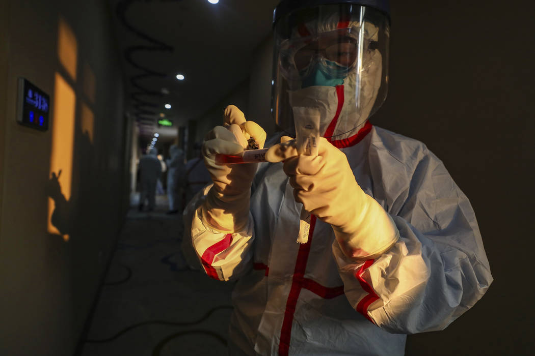 A medical worker in a protective suit writes on a tube after collecting a sample for nucleic ac ...