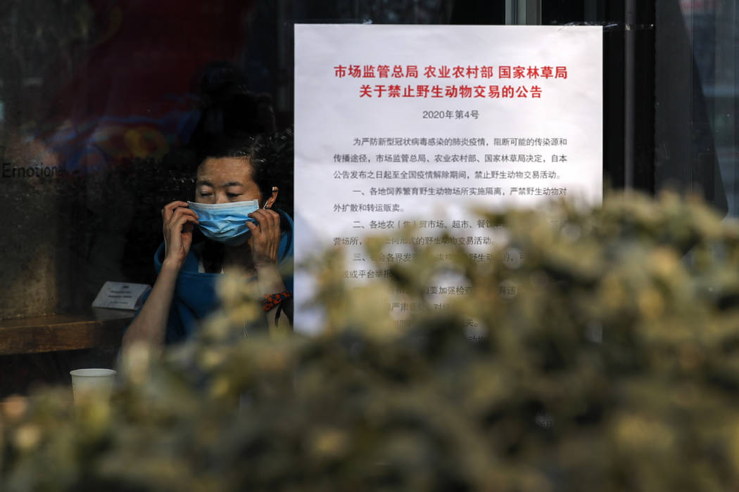 A woman puts on a mask near a notice board that reads "Bans on wild animals trading follow ...