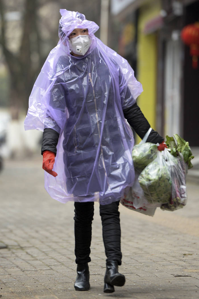 A masked woman wearing a raincoat carrying foods in Wuhan in central China's Hubei province, Mo ...