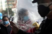 A man wearing a protective face mask covered himself with a plastic cover before enters a super ...