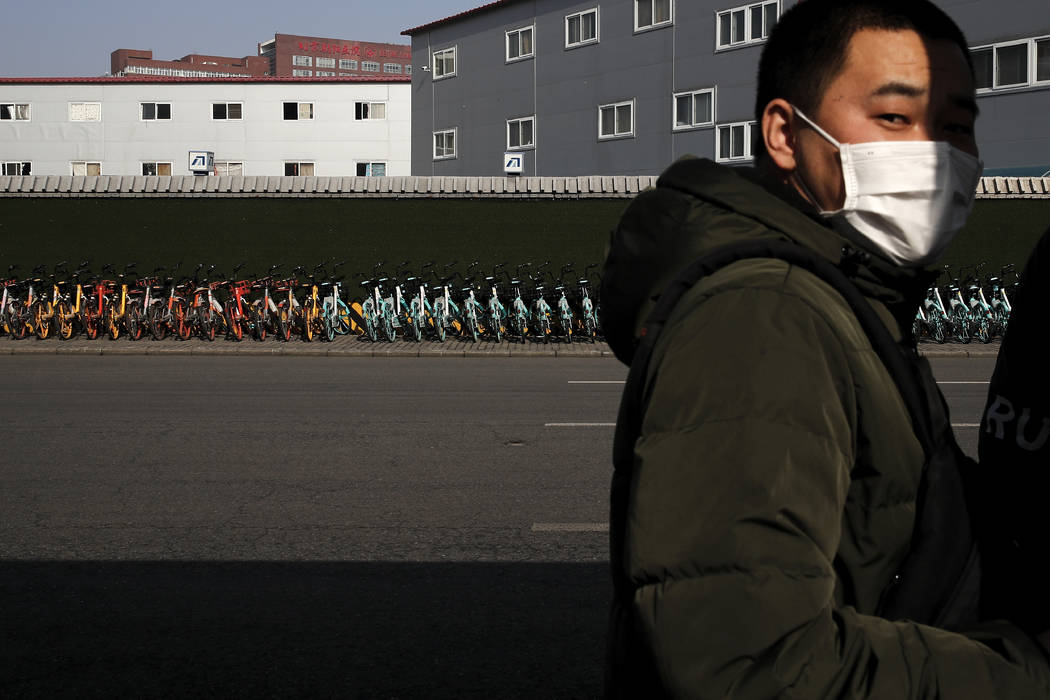A man wearing a mask stands near a pile of bicycles from bike-sharing companies parked outside ...