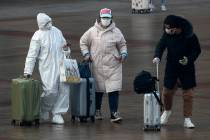 A passenger wearing a full-body protective suit catches the eyes of others as they walk out fro ...