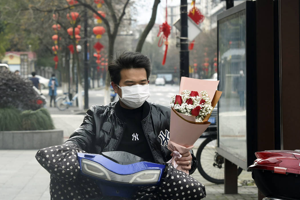 A man wearing a face mask carries a Valentine's Day bouquet as he rides a scooter in Hangzhou i ...