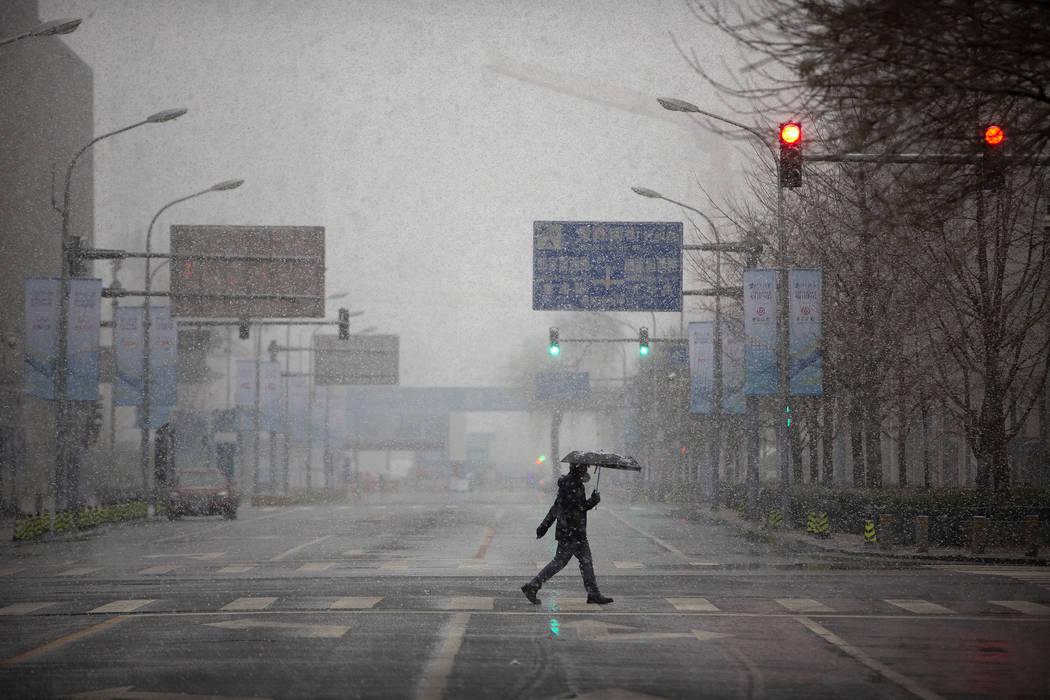 A man wears a mask as he walks across an empty intersection during the morning rush hour as sno ...