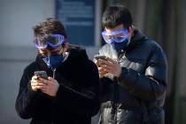 Travelers wear face masks and goggles as they use their smartphones outside the Beijing Railway ...
