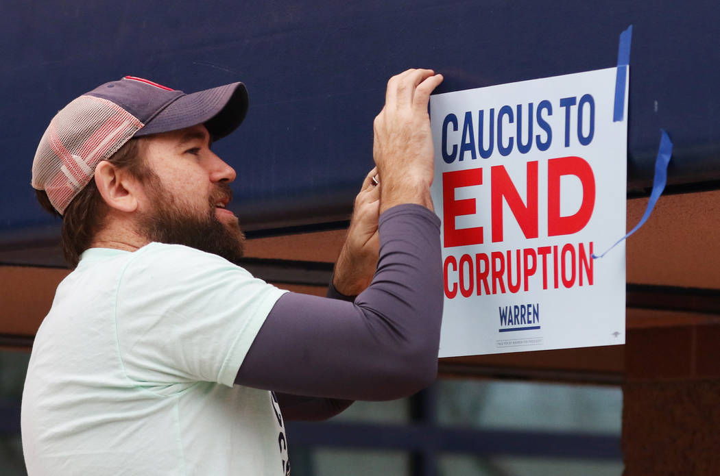 David Hohman, a volunteer for Elizabeth Warren campaign, puts sign as Democratic caucus-goers s ...