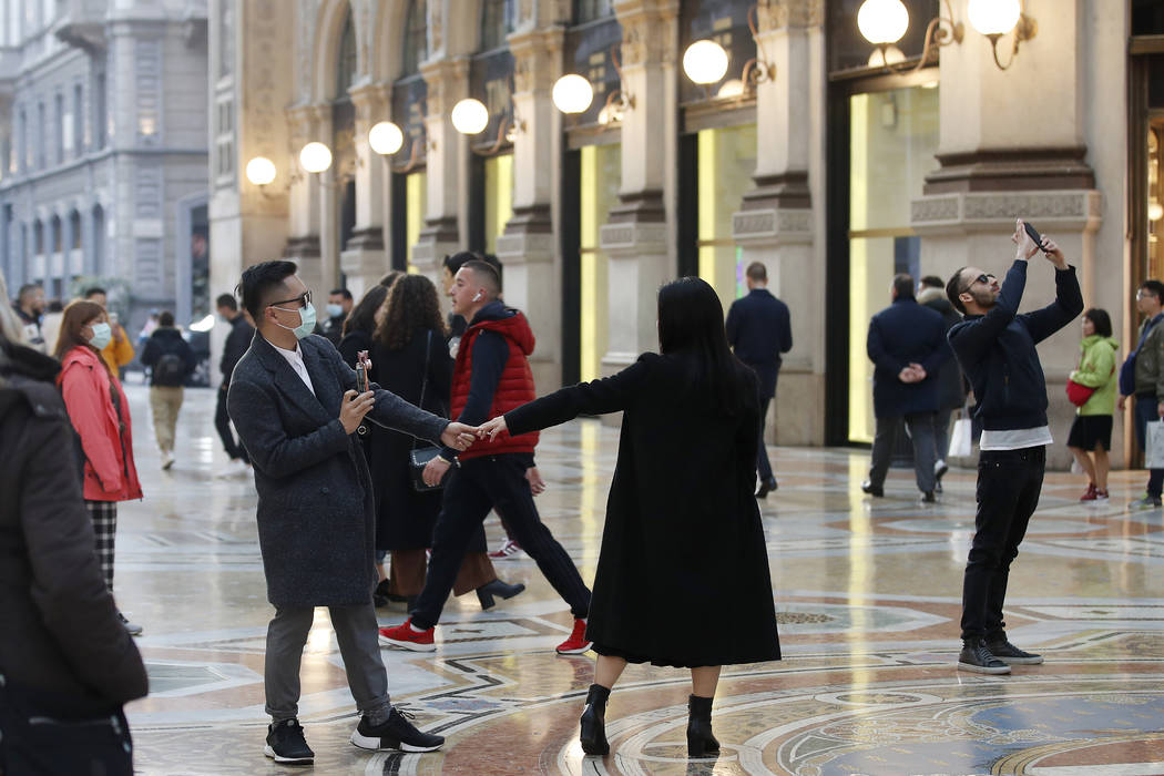 Tourists wearing sanitary masks move a few steps of dance, in downtown Milan, Italy, Sunday, Fe ...