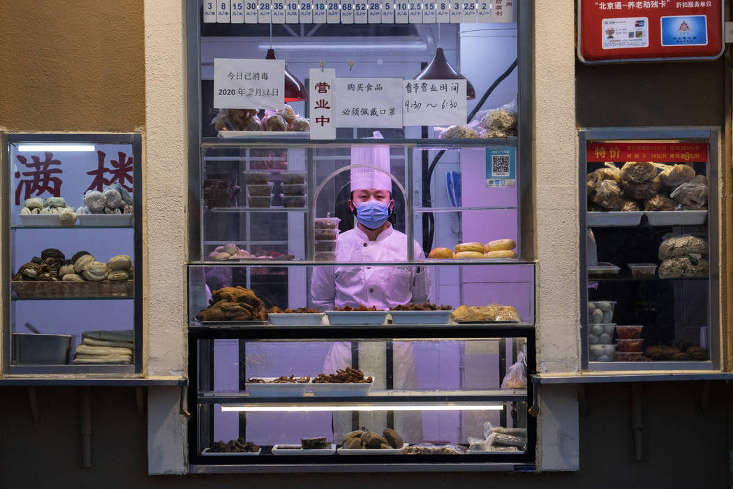 a chef looks out from behind a display of food products at a restaurant in Beijing, China, Satu ...