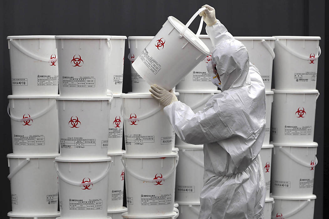 A worker in protective gear stacks plastic buckets containing medical waste from coronavirus pa ...
