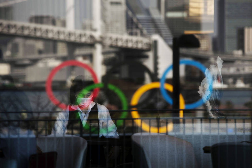 The Olympics rings are reflected on the window of a hotel restaurant as a server with a mask se ...