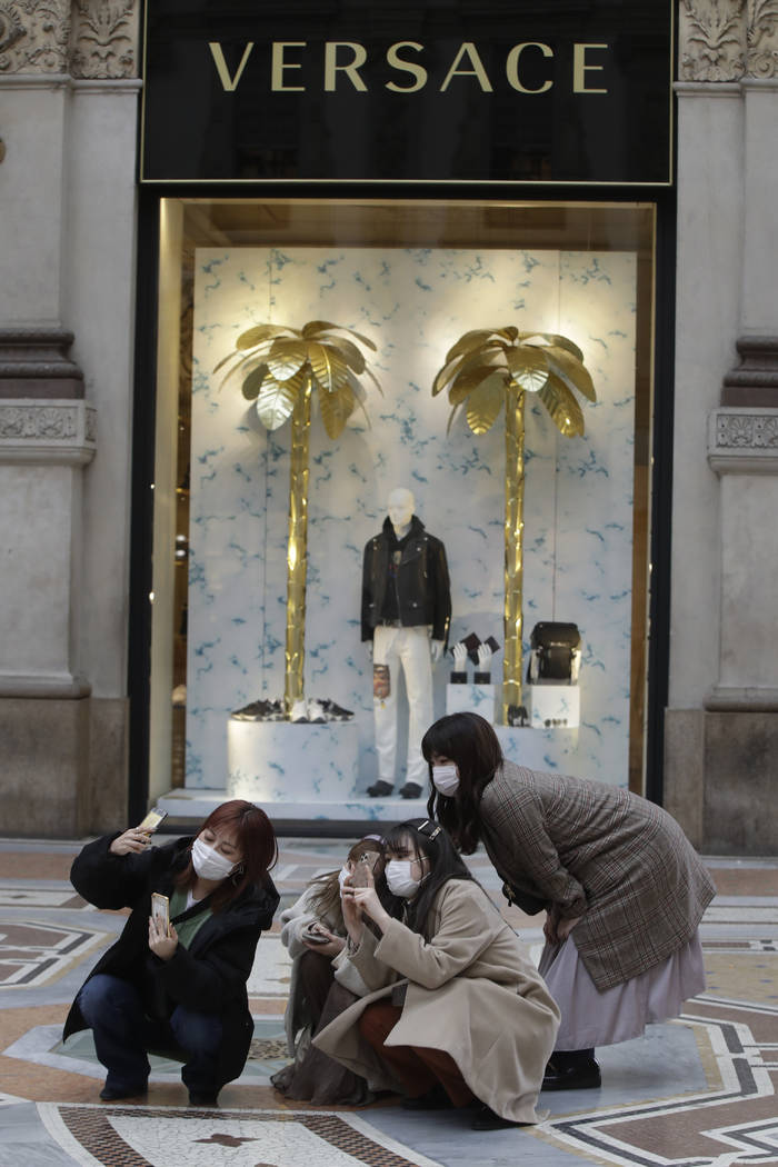 Tourists, wearing face masks, pose for a selfie in front of a Versace shop window in downtown M ...