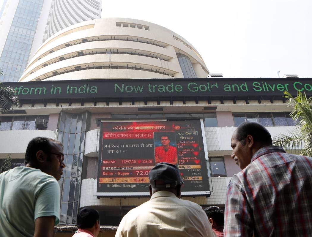 People watch a display screen outside the Bombay Stock Exchange (BSE) in Mumbai, India, Friday, ...
