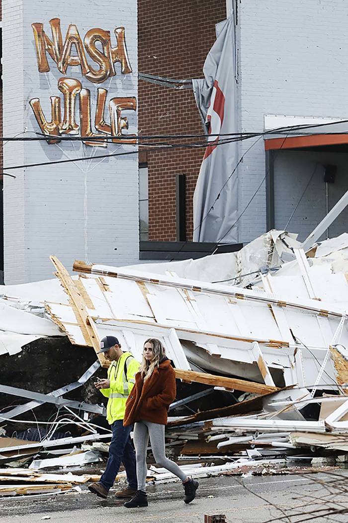 People walk past storm debris following a deadly tornado, Tuesday, March 3, 2020, in Nashville, ...