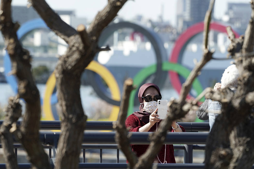A tourist wearing a protective mask takes a photo with the Olympic rings in the background Tues ...