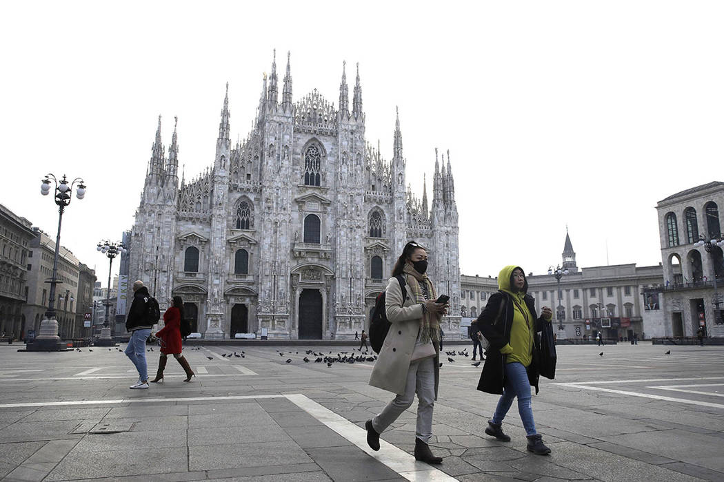 A woman wearing a sanitary mask walks past the Duomo gothic cathedral in Milan, Italy, in Febru ...