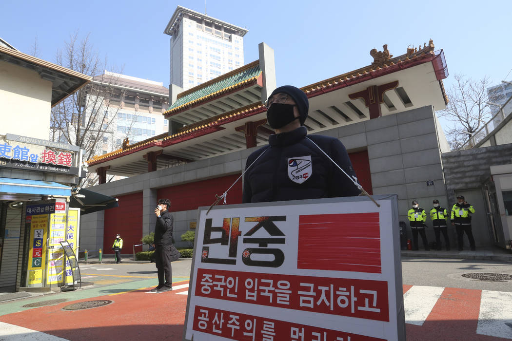 A man wearing a face mask stands calling for a ban on Chinese people entering South Korea near ...