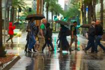 People cross the street on a rainy day about the Fremont Street Experience and South 3rd Street ...