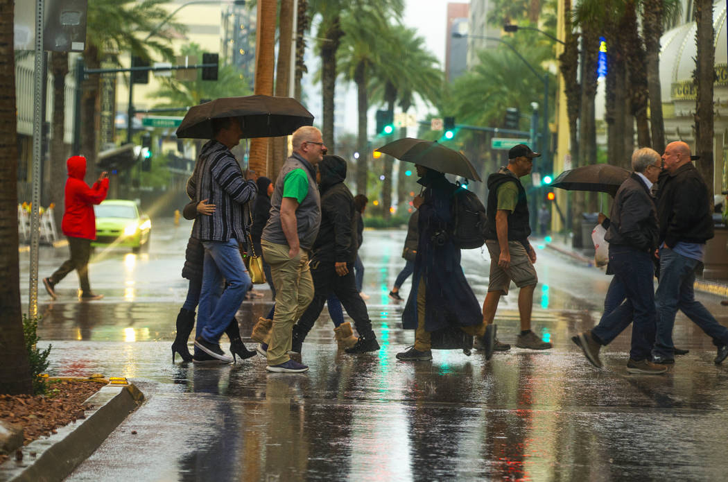 People cross the street on a rainy day about the Fremont Street Experience and South 3rd Street ...