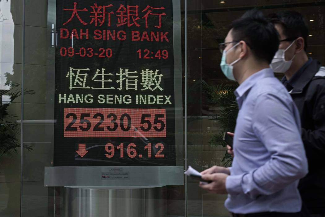 People walk past an electronic board showing Hong Kong share index outside a local bank in Hong ...