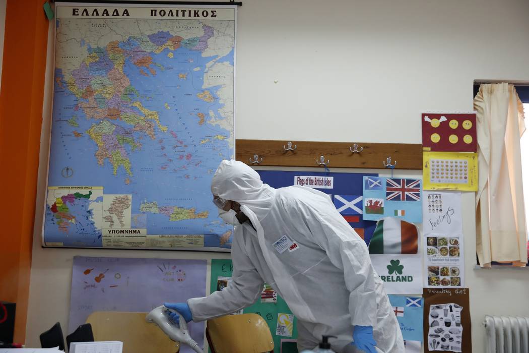 A worker wearing protective suit sprays disinfectant inside a classroom at a primary school in ...