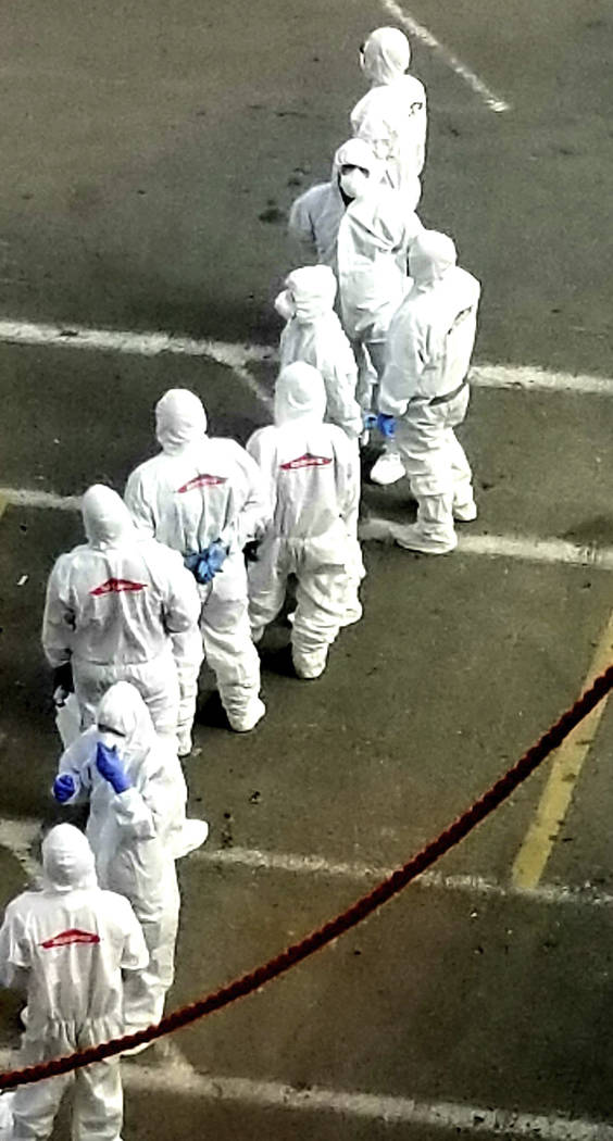 In this photo provided by Michele Smith, a crew from the Grand Princess in protective gear wait ...