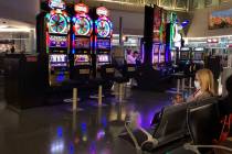 A passenger wearing a mask, right, sits about one of the near empty slot machine areas in Conco ...