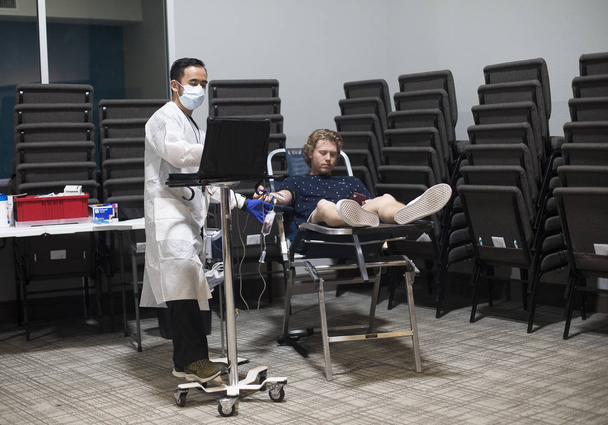 Ernesto Perez, a phlebotomist tech and supervisor, helps William Buening, 17, as he gives blood ...