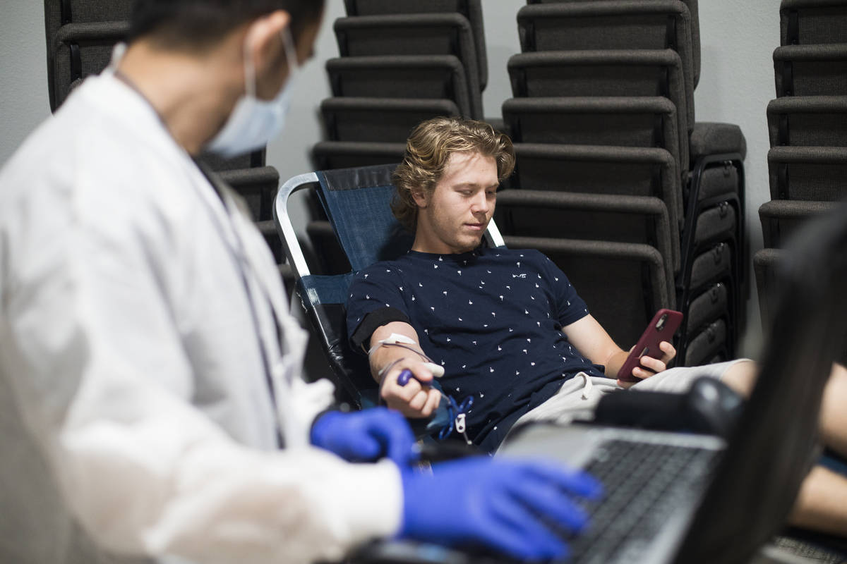 Ernesto Perez, a phlebotomist tech and supervisor, helps William Buening, 17, as he gives blood ...