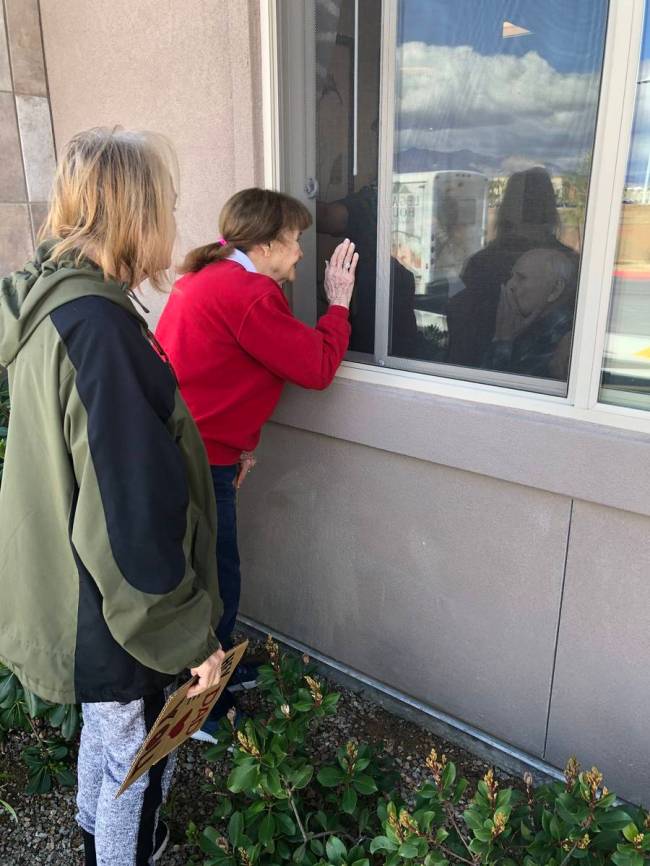 Judy and Jan Swanson visit their family member, Mel Swanson, outside his window at his assisted ...