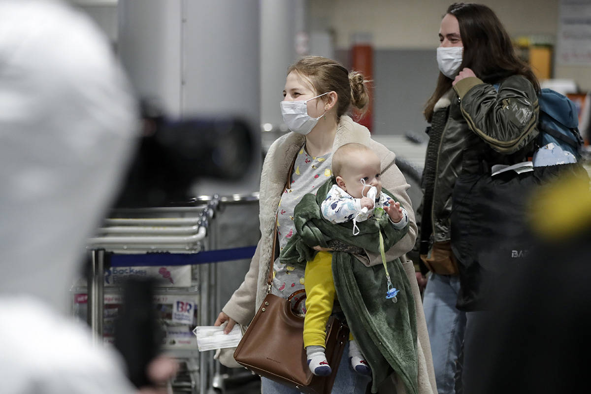 A passengers wearing face mask with her baby walks to medical experts to be checked after arriv ...
