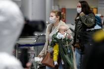 A passengers wearing face mask with her baby walks to medical experts to be checked after arriv ...