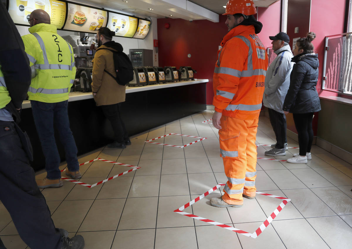 People stand in marked places to keep a social distance at a fast food restaurant in London, Fr ...