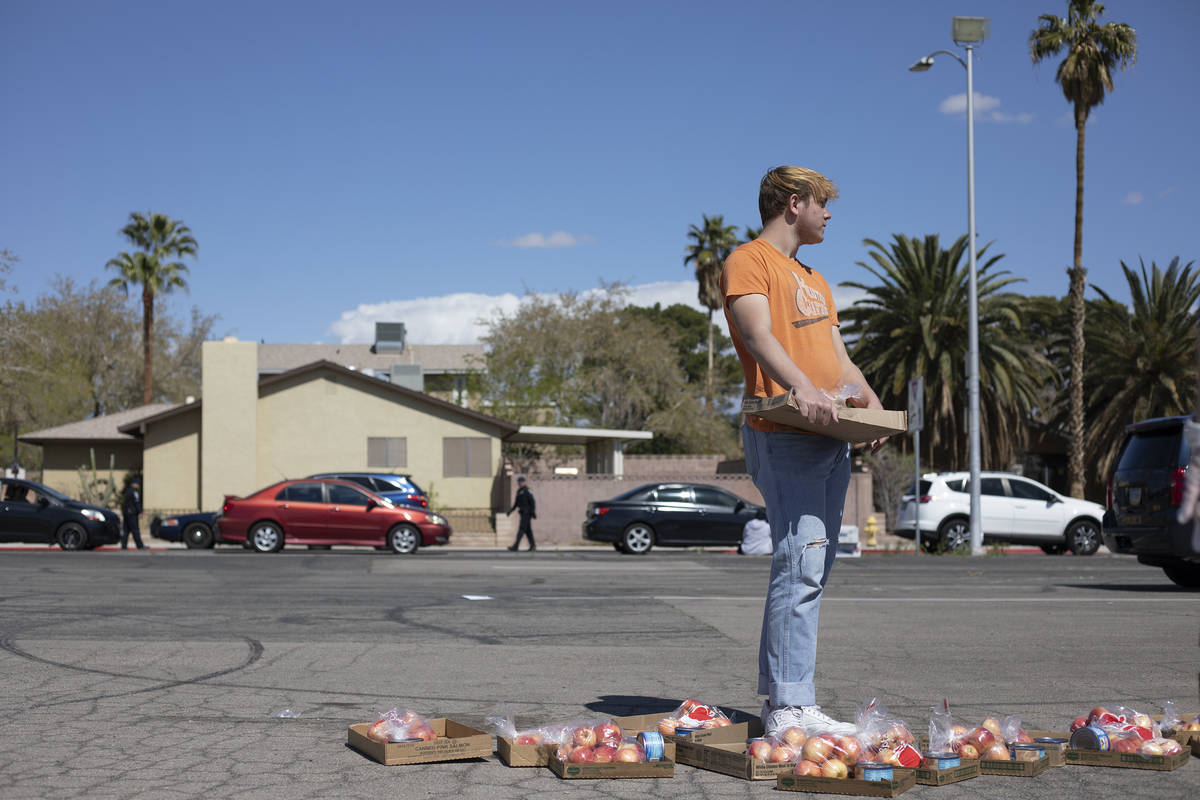 Nicklaus Kane, a volunteer with The Just One Project, waits to put apples in car trunks at a fo ...