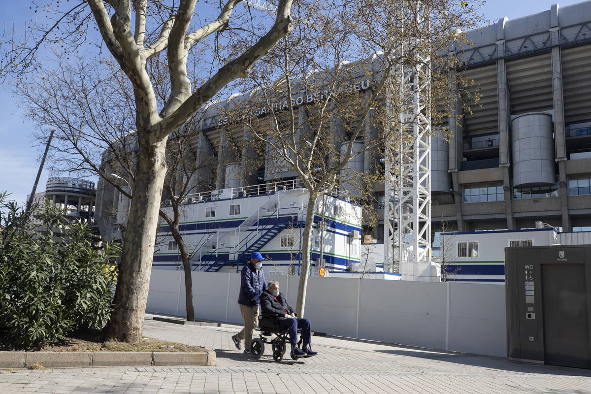 A man is pushed in the wheelchair while wearing protective masks near Real Madrid's Santiago Be ...