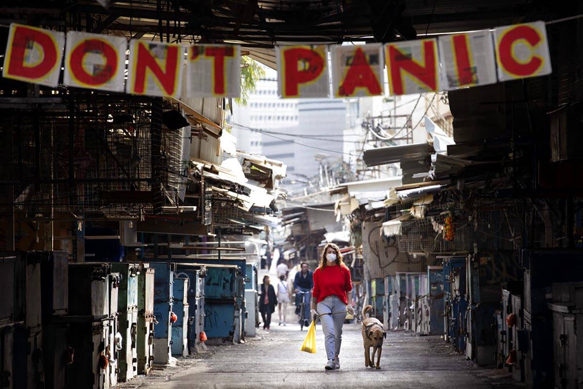A woman walks her dog under a "don't panic" sign hanging on the entrance of a food ma ...