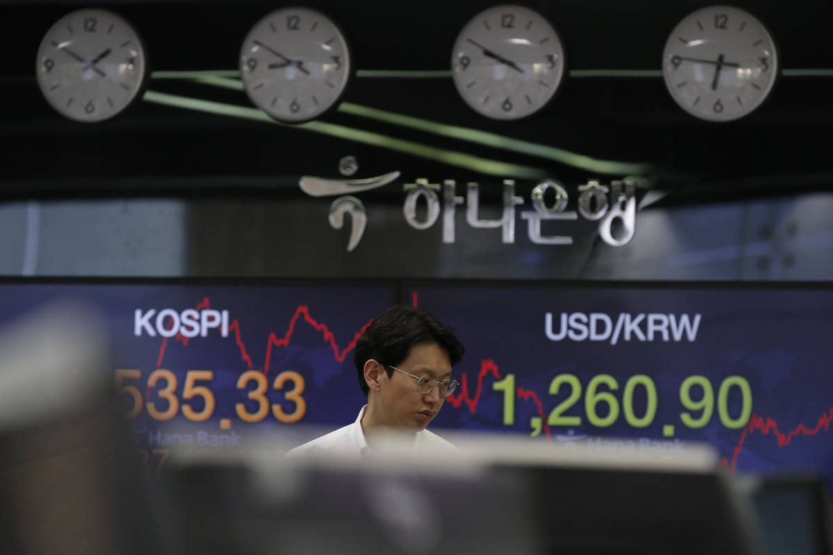 A currency trader walks by screens showing the Korea Composite Stock Price Index (KOSPI), left, ...