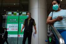 People wearing face masks walk past a bank electronic board showing the Hong Kong share index a ...