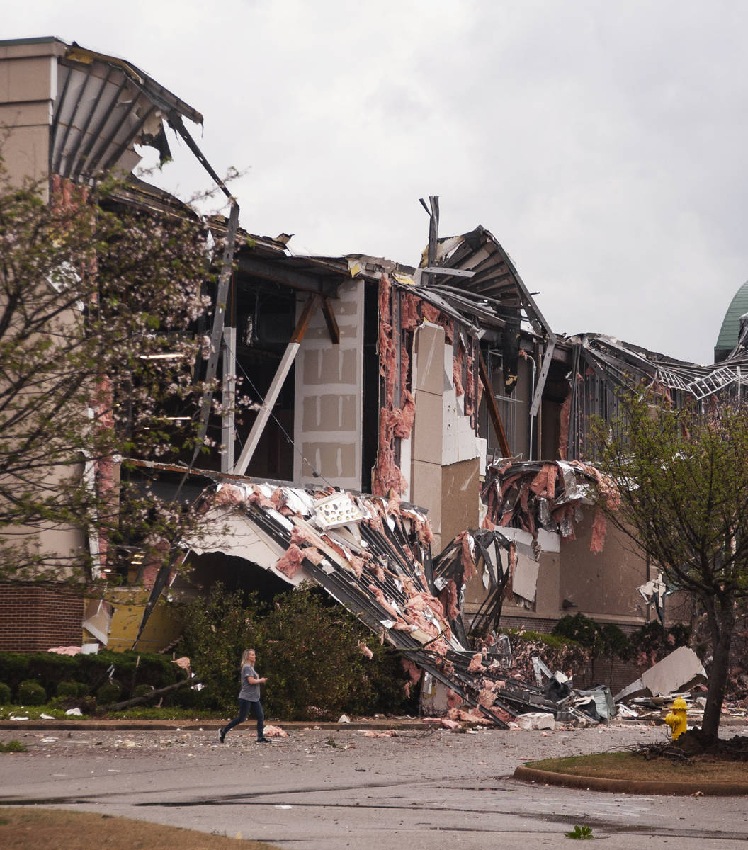 A person walks past the damage to the rear side of a Dillard's store after a tornado struck Sat ...