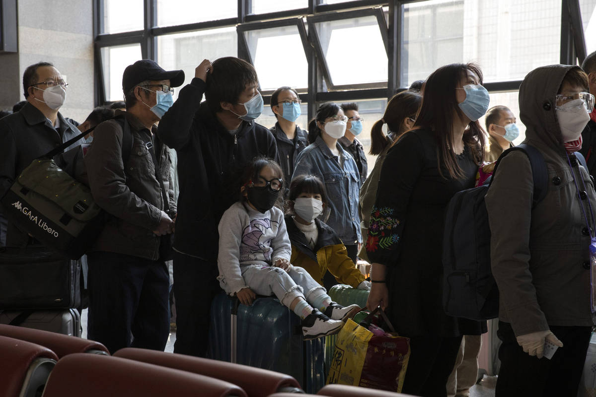Travelers wearing face masks to help curb the spread of the coronavirus line up for their train ...